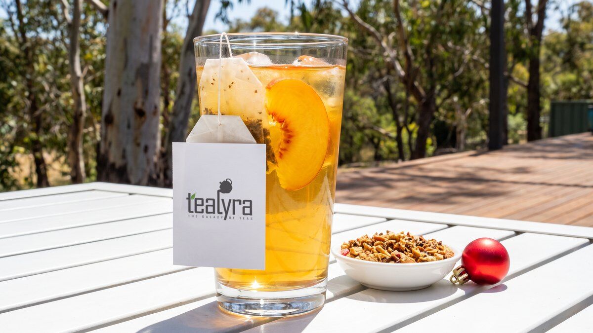 Tall glass of peach iced tea with a Tealyra tea bag tag on an outdoor table in Australian summer sun