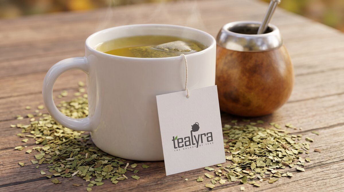 A white mug of yerba mate with a Tealyra tea tag, loose green yerba mate and a calabash gourd with a bombilla